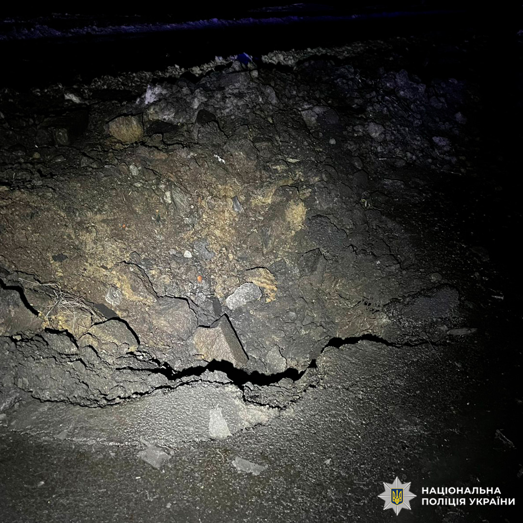 Пошкоджена ділянка дороги з тріщинами та уламками асфальту.