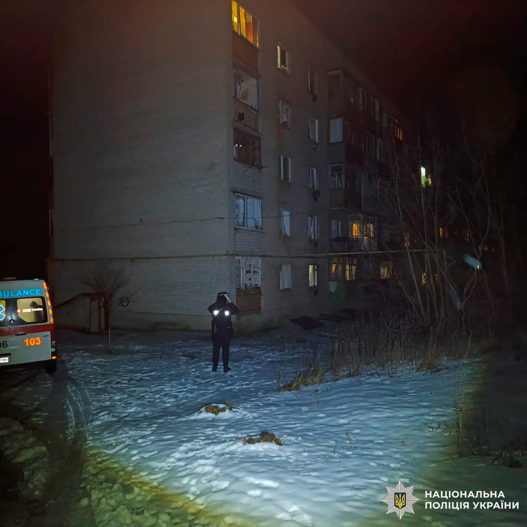 Нічна сцена біля житлового будинку. На місці присутні швидка допомога та представник Національної поліції України.