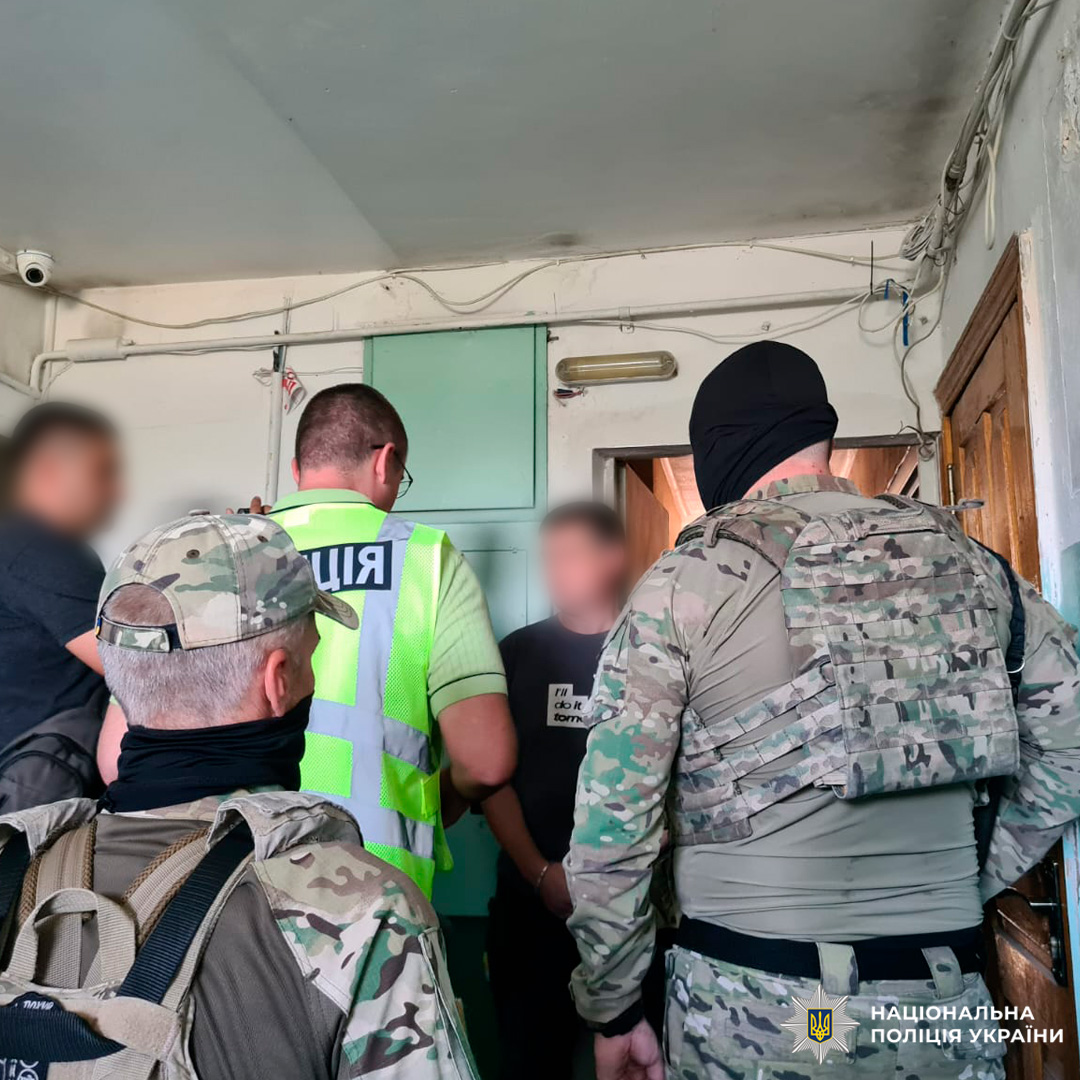Працівники Національної поліції України проводять затримання у приміщенні. Підозрюваний у кайданках, поруч кілька правоохоронців у формі та камуфляжі.