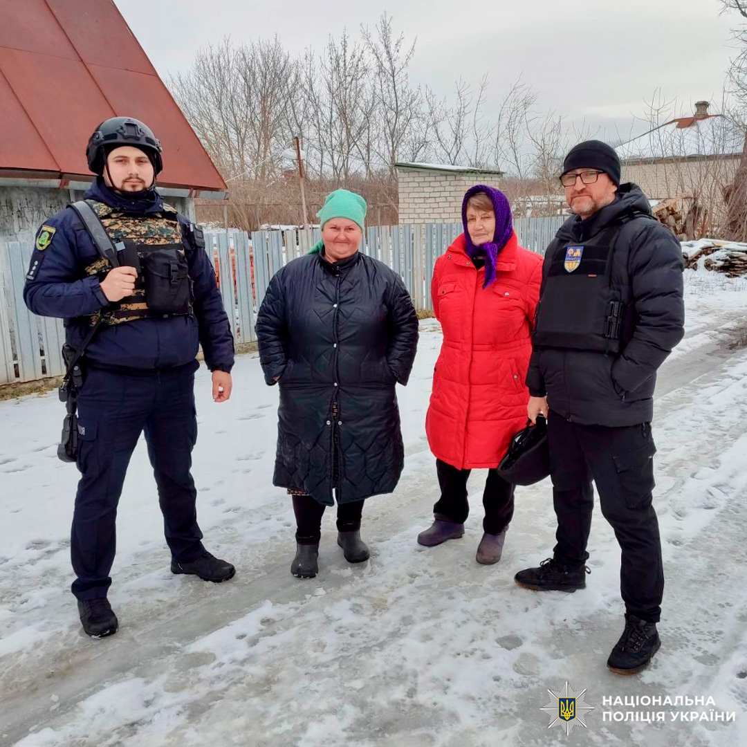 Поліцейські у тактичному спорядженні спілкуються з двома літніми жінками на засніженій стежці біля житлових будинків.