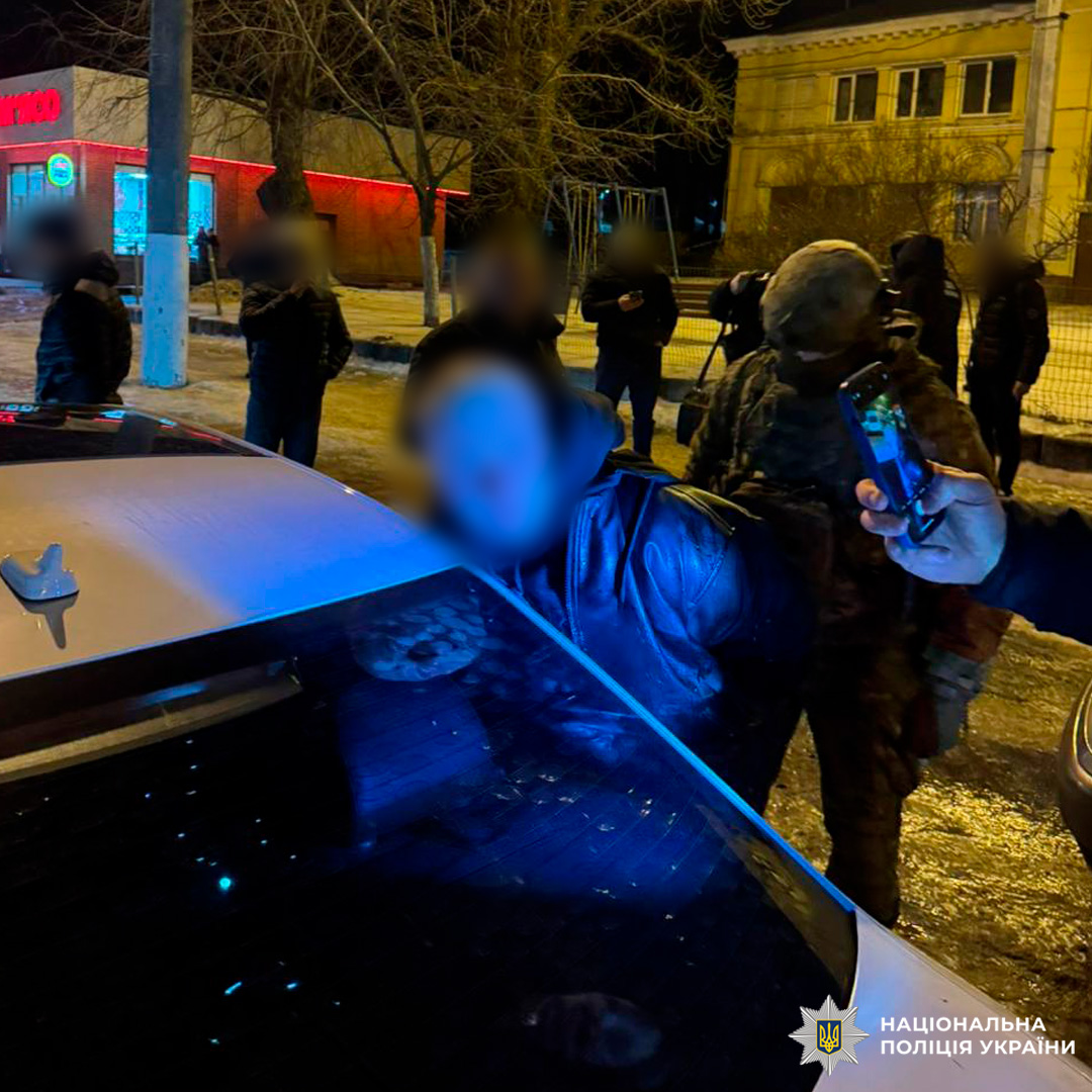 Поліцейські у тактичному спорядженні проводять операцію: підозрюваного притиснуто до багажника автомобіля, поруч - інші учасники події.