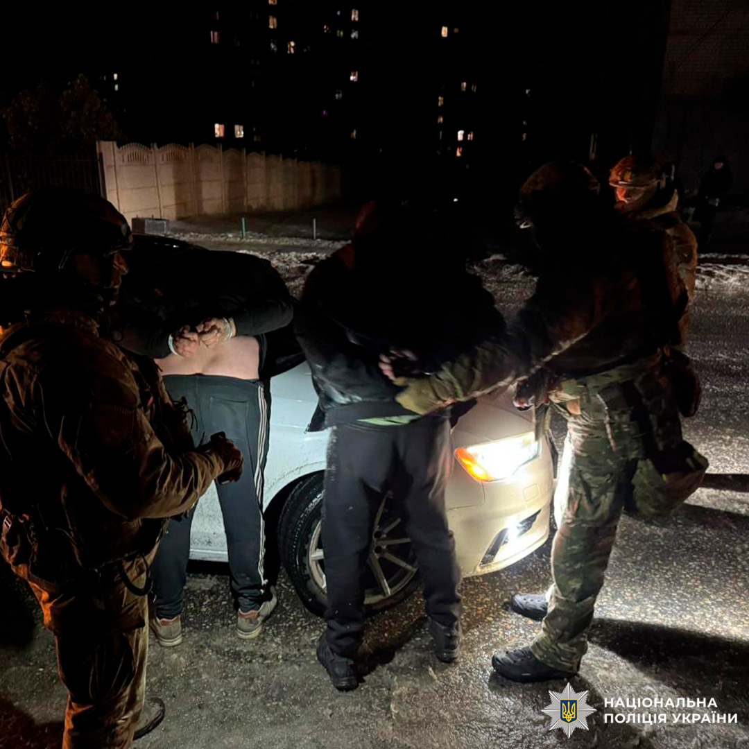 Поліцейські у тактичному спорядженні проводять операцію: підозрюваного притиснуто до багажника автомобіля, поруч - інші учасники події.