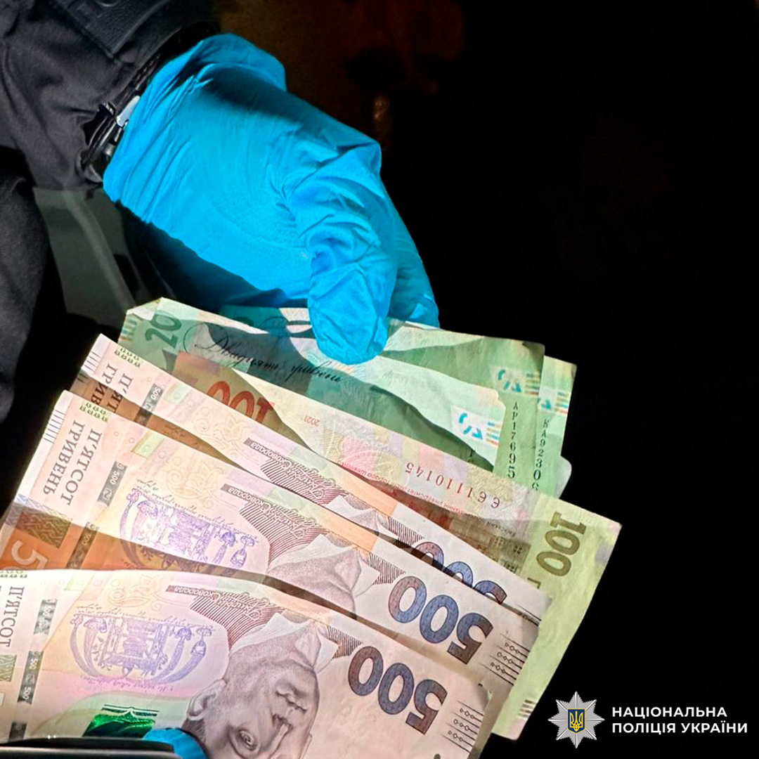 Поліцейський у рукавичках демонструє купюри різних номіналів, зафіксовані як речові докази.