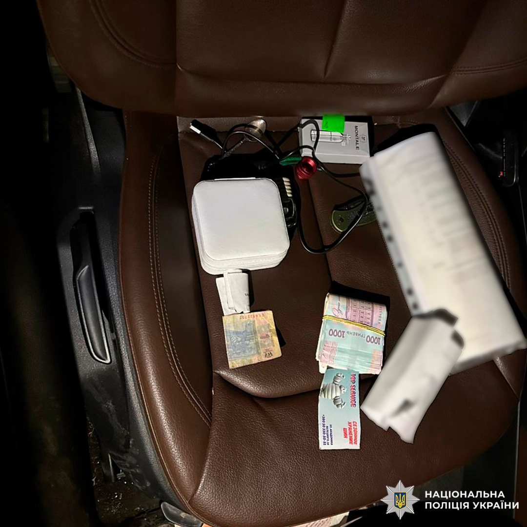 На передньому сидінні автомобіля розкладені купюри, електронні пристрої та інші речі, зафіксовані як речові докази.