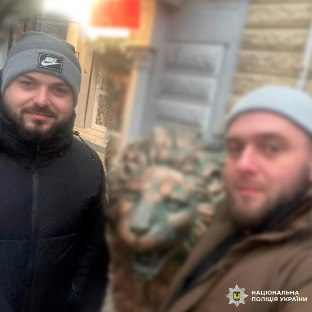 Двоє осіб у зимовому одязі біля декоративної скульптури лева.