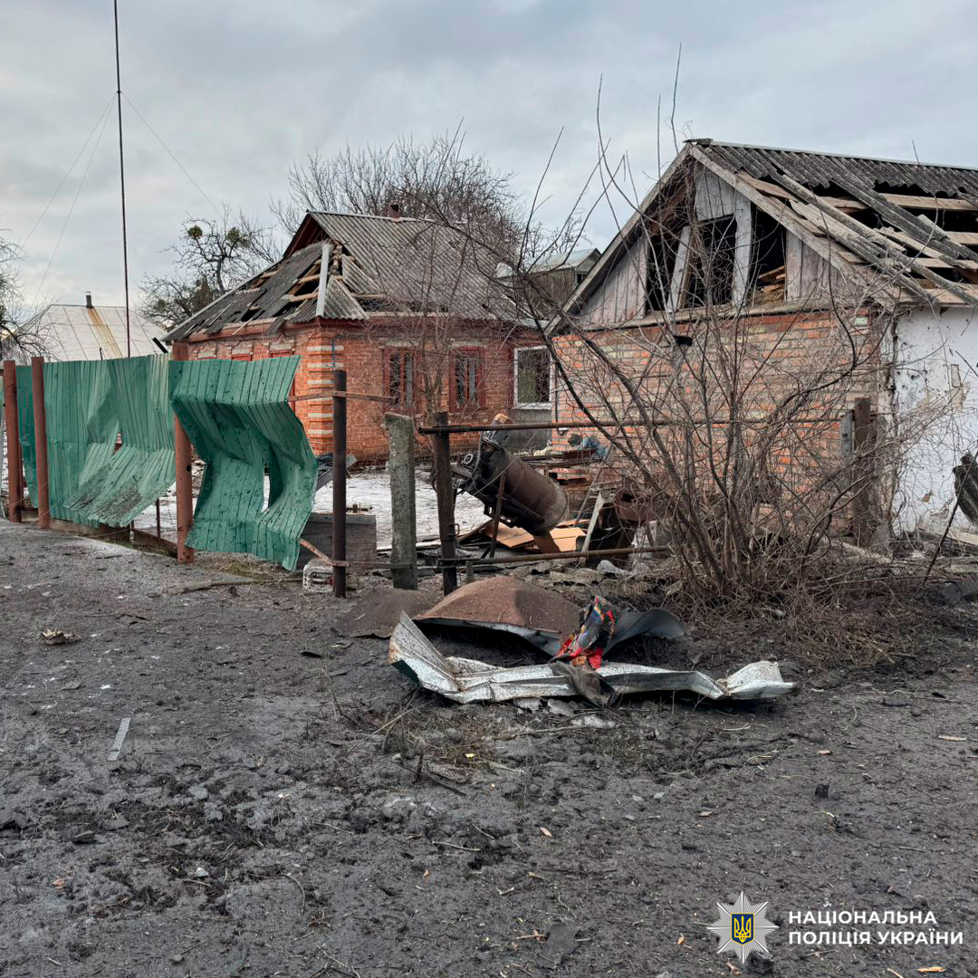 Два житлові будинки з пошкодженими дахами та зруйнованим подвір’ям після вибуху. На передньому плані - уламки металу.