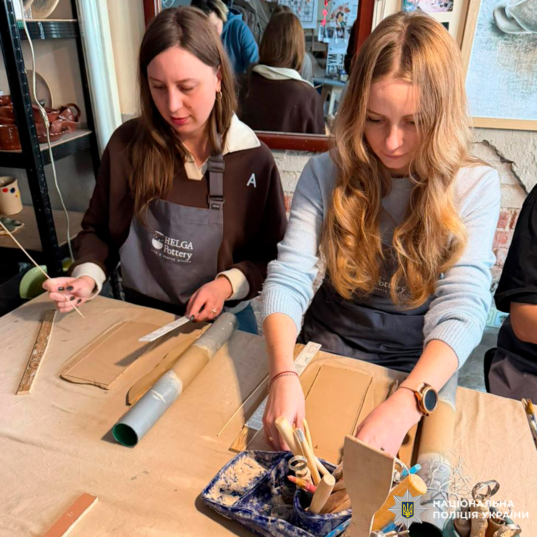 Двоє учасників майстерні працюють із глиною за столом, використовуючи інструменти для формування.