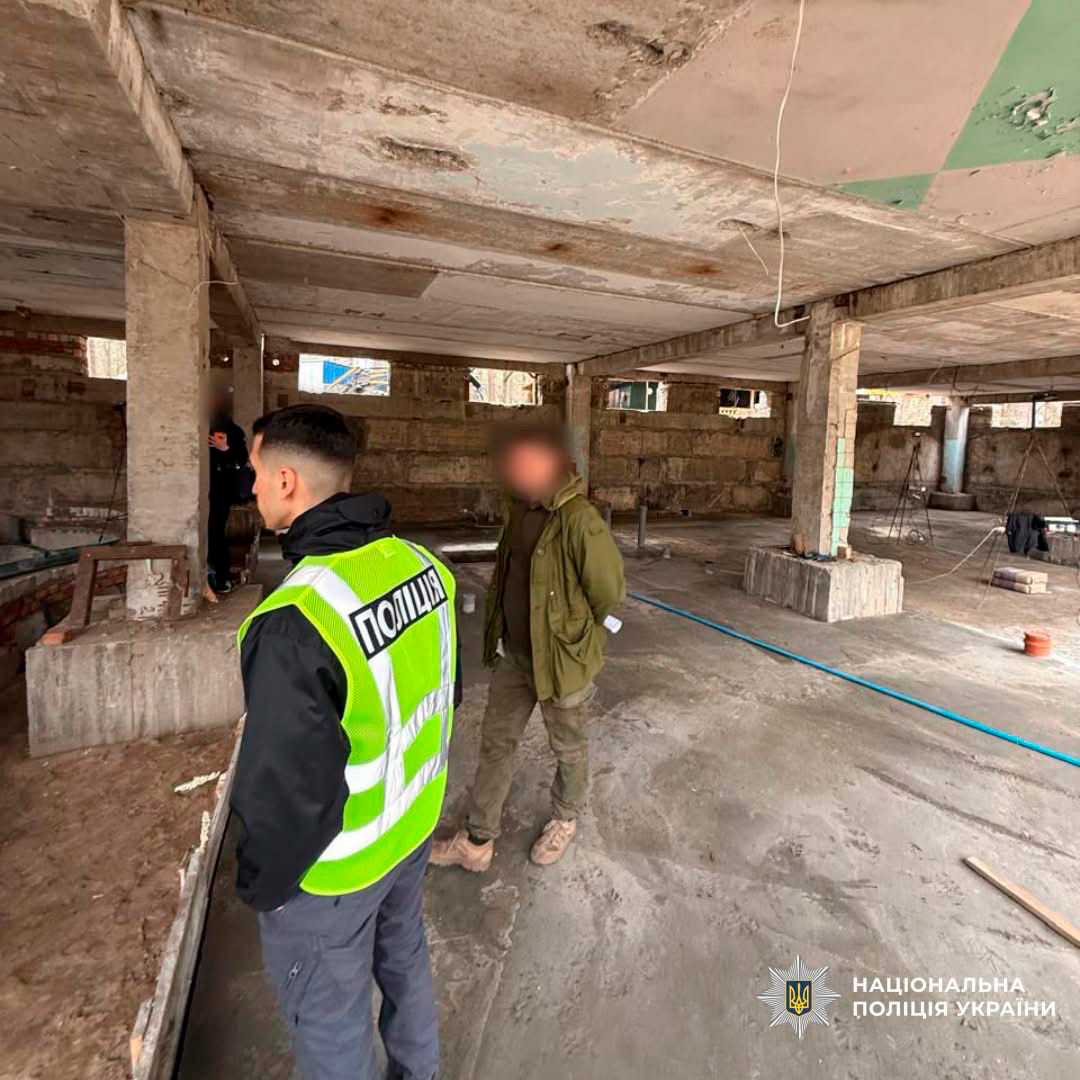 Працівник поліції проводить огляд недобудованої будівлі разом із громадянином. Усередині видно бетонні конструкції та будівельні матеріали.