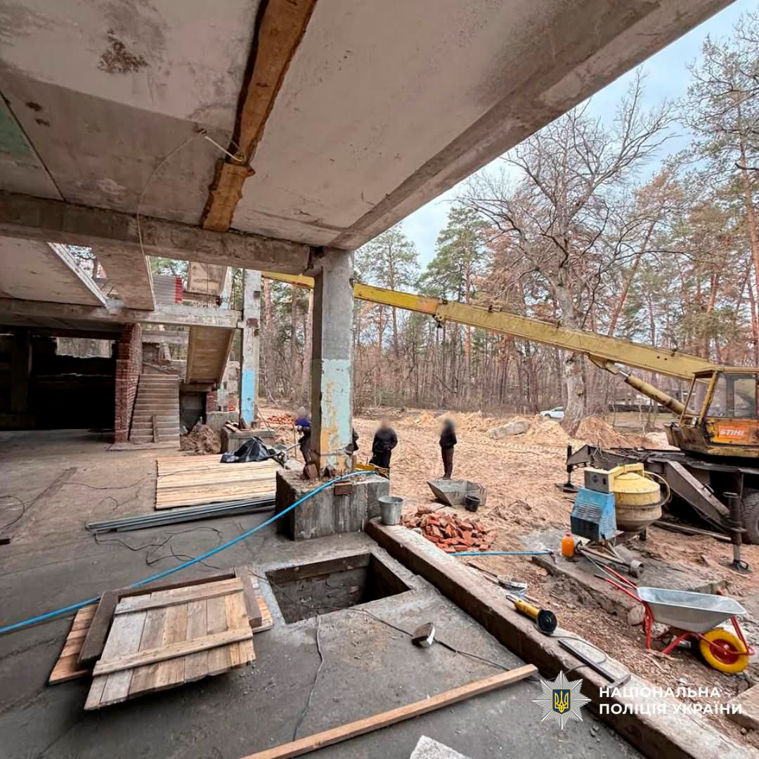 Поліцейські здійснюють огляд території біля недобудованої споруди. На майданчику видно кран, будівельні матеріали та інструменти.