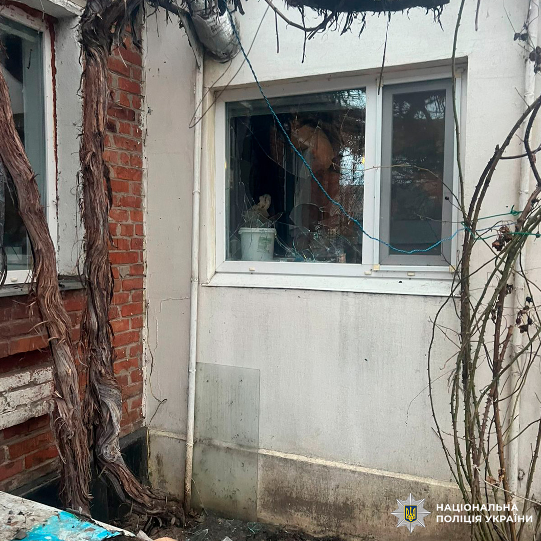 Будівля з розбитим вікном і тріснутим склом, на стіні видно сухі гілки та мотузку. Усередині кімнати - відро та інші предмети.