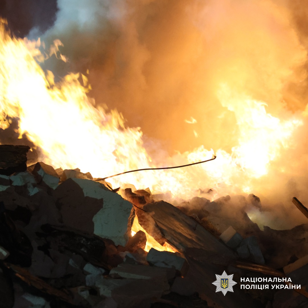 Пожежа у будівлі вночі: рятувальники та поліцейські працюють на місці події, серед уламків та густого диму.