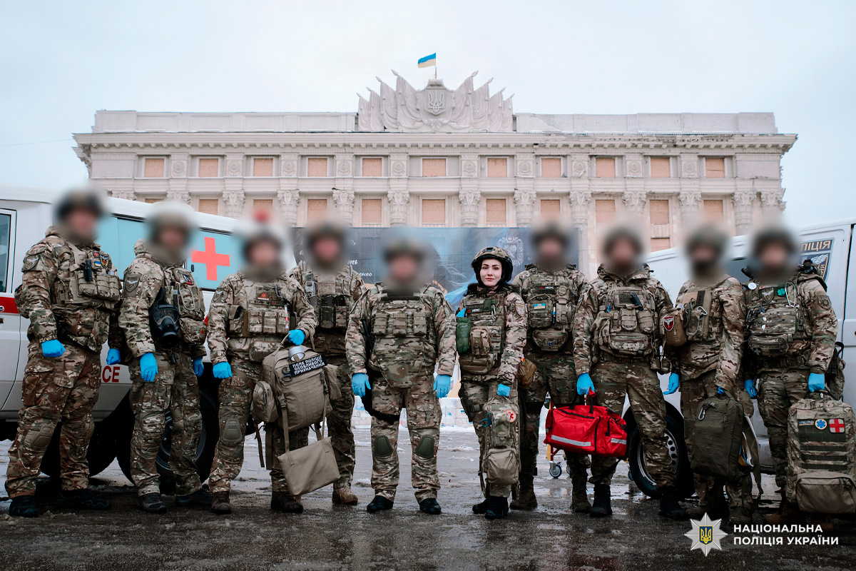 Група співробітників у камуфляжній формі з медичними сумками та спорядженням стоїть перед урядовою будівлею. На задньому плані - автомобілі швидкої допомоги.