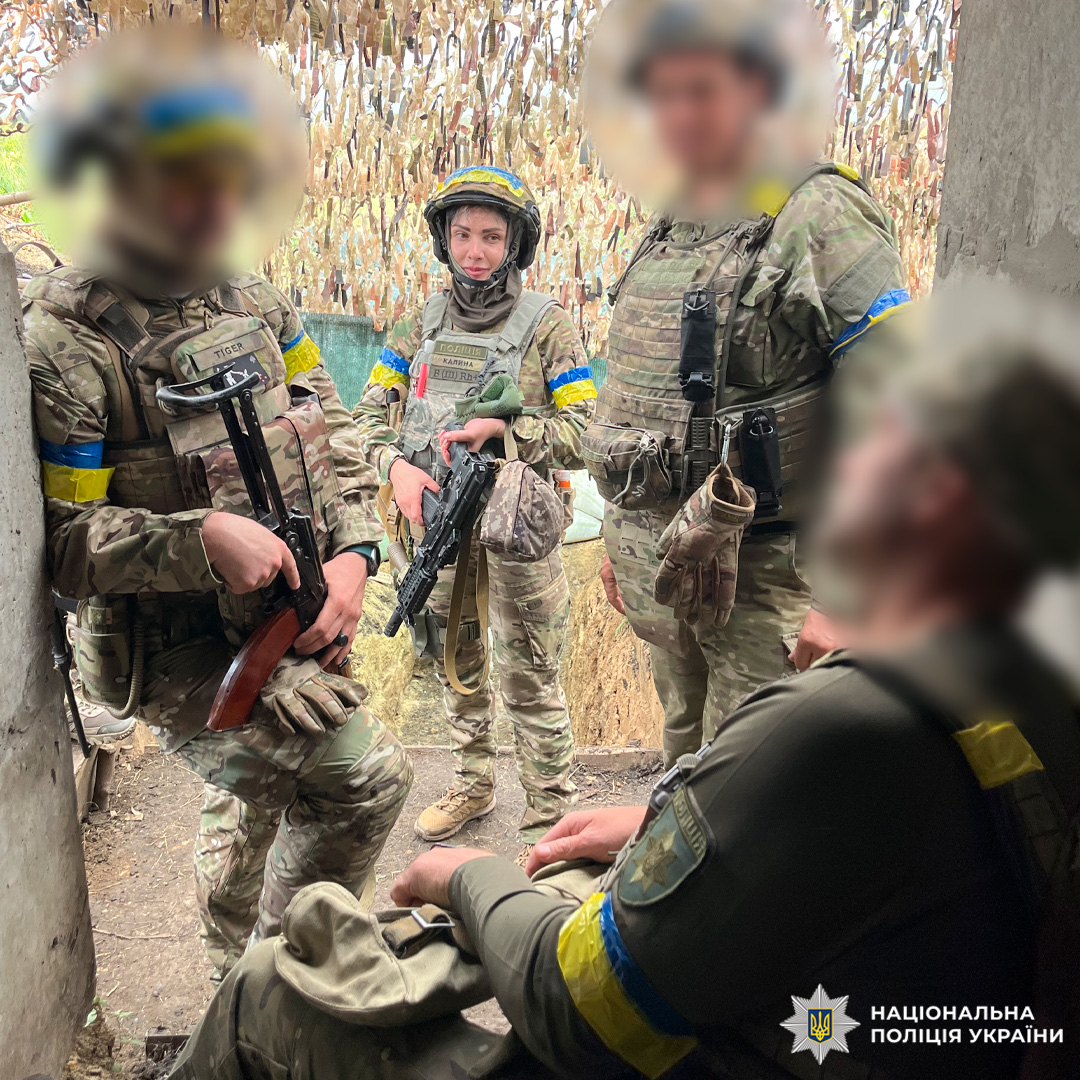 Група поліцейських у камуфляжі з синьо-жовтими пов’язками перебуває в укритті, один із них тримає зброю з написом “Герої не вмирають”.