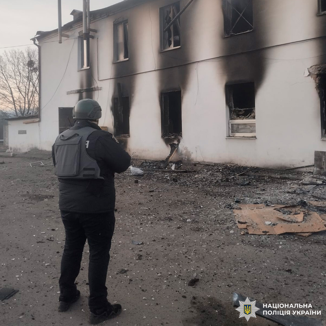 Працівник Національної поліції України у захисному спорядженні проводить огляд місця події біля знищеного транспортного засобу.