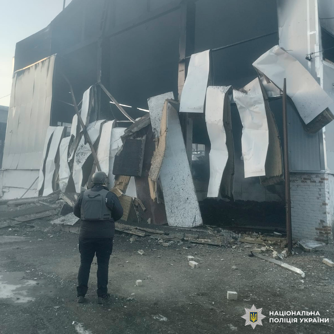 Працівник Національної поліції України у захисному спорядженні проводить огляд місця події біля знищеного транспортного засобу.