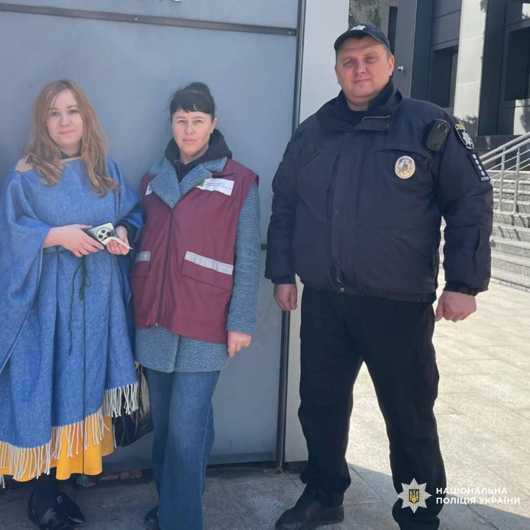 На цьому фото зображено групу людей на вулиці, серед яких є представник Національної поліції України.