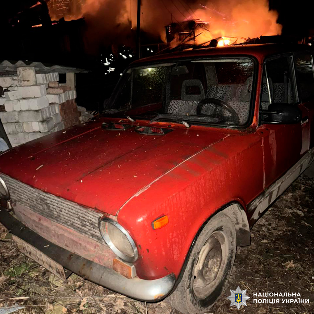 Поліція працює біля палаючої будівлі; поруч - червоний автомобіль серед уламків.