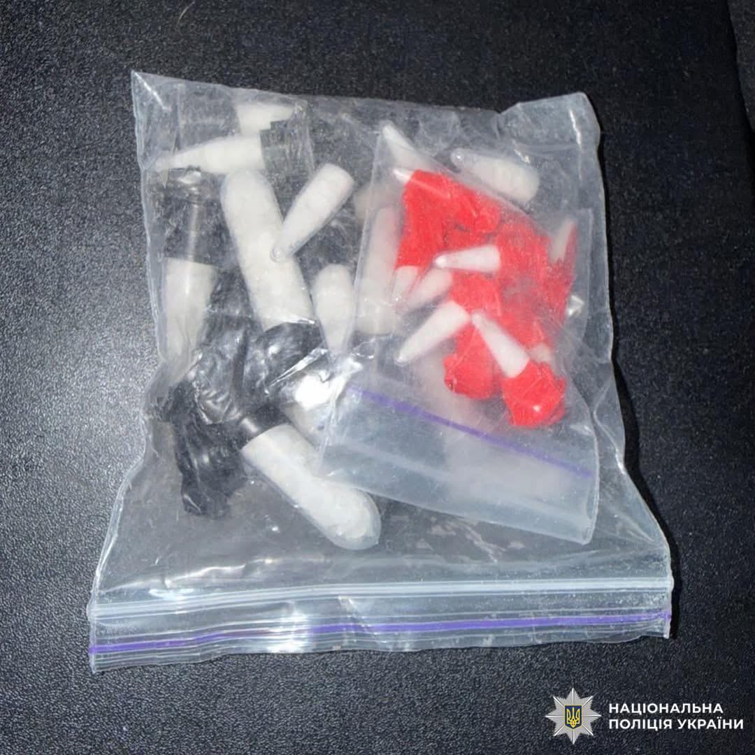 Прозорий пакет із циліндричними предметами різних кольорів, розташований на темній поверхні.