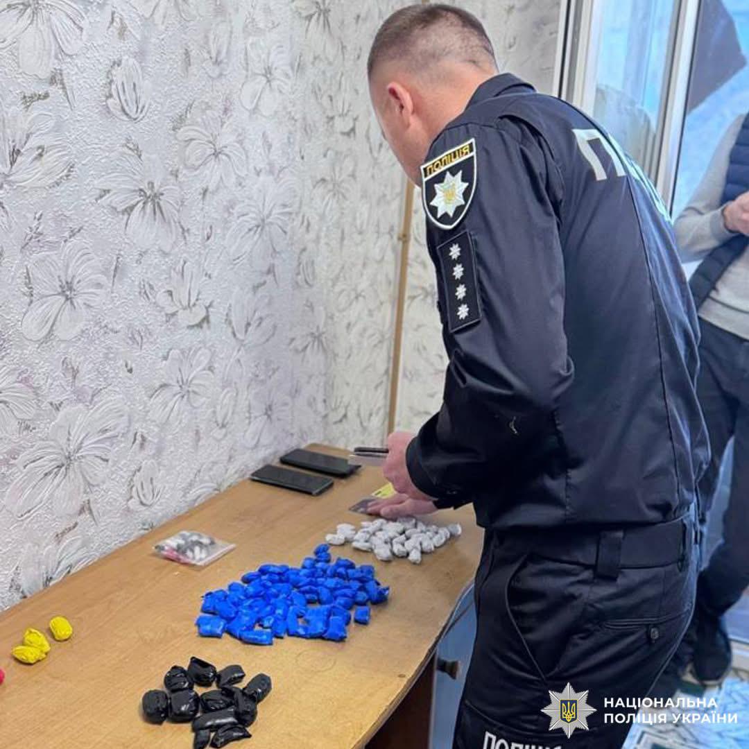 Поліцейський у формі оглядає пакети різних кольорів, мобільні телефони та інші предмети на столі.