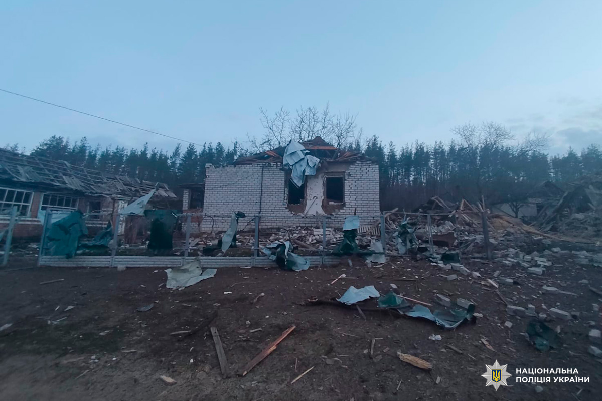 Зруйнований житловий квартал: центральний цегляний будинок із частково обваленим дахом, навколо уламки металу, дерева та цегли.