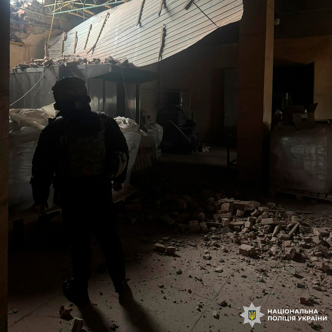 Інтер’єр пошкодженої будівлі: уламки цегли та бетону на підлозі, частково обвалена стеля, співробітник у тактичному спорядженні оглядає приміщення.