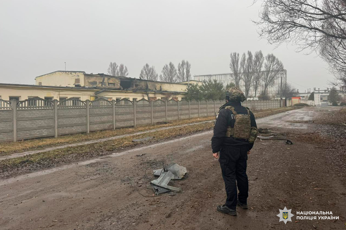 Співробітник у формі поліції оглядає пошкоджену будівлю з ознаками пожежі та руйнувань, поруч уламки обладнання.