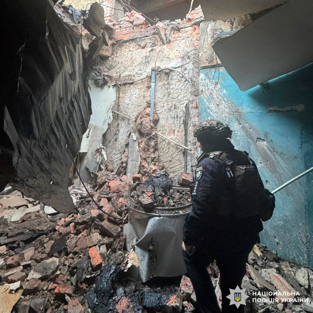 Інтер’єр пошкодженої будівлі: обвалені стіни, уламки на підлозі, співробітник у тактичному спорядженні оглядає приміщення.