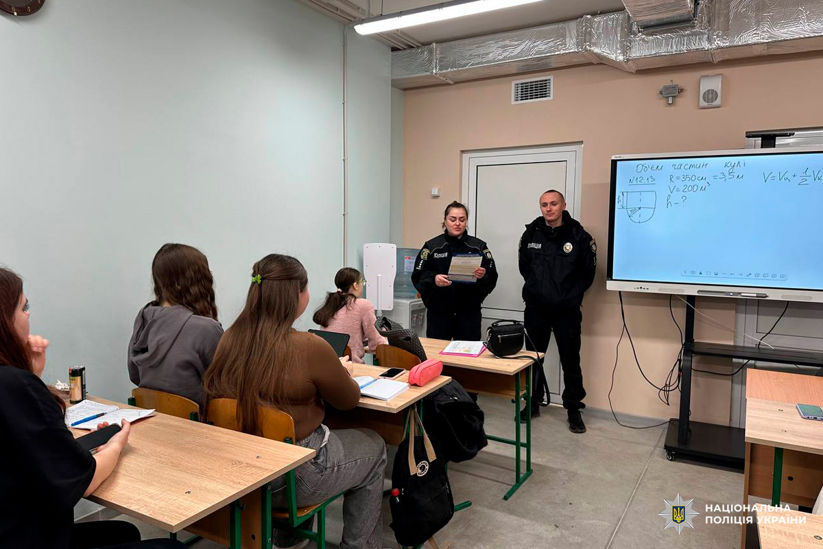 У класі кілька учнів сидять за партами, перед ними двоє офіцерів Національної поліції України у формі. Один тримає документ і виступає, інший стоїть поруч. На дошці видно математичну задачу з об’ємом частини кулі та схему.