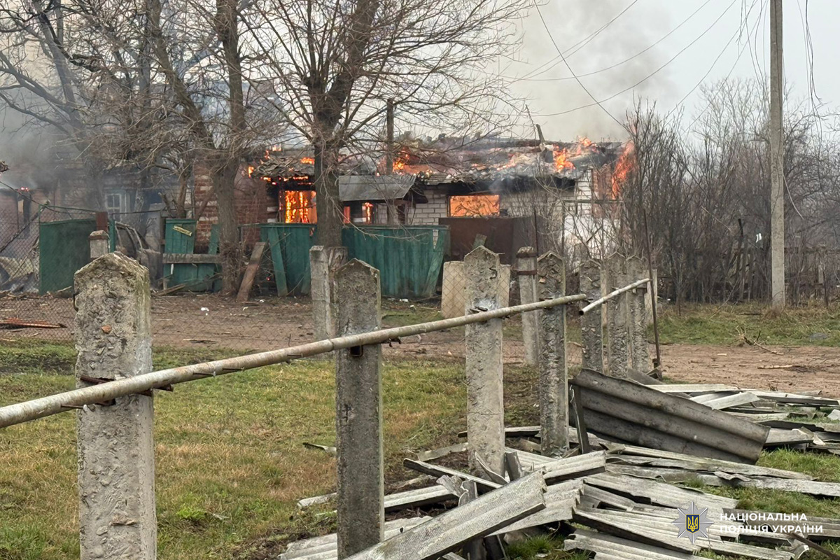 Будинок у Харківській області охоплений вогнем, дах і приміщення палають, густий дим здіймається вгору. На передньому плані видно зруйновану огорожу та уламки.