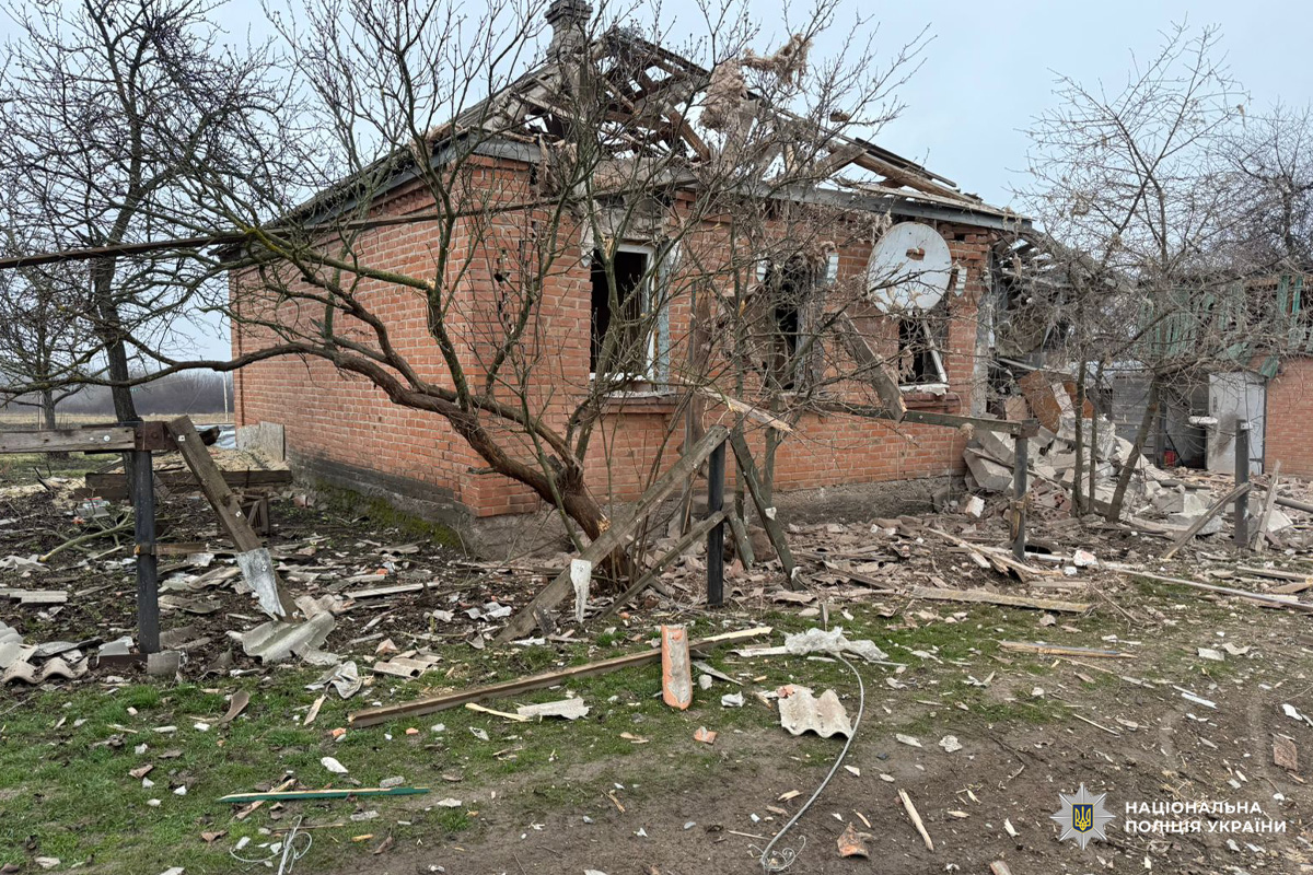 Пошкоджений житловий будинок із зруйнованим дахом та розбитими вікнами, уламки деревини й цегли розкидані на подвір’ї.