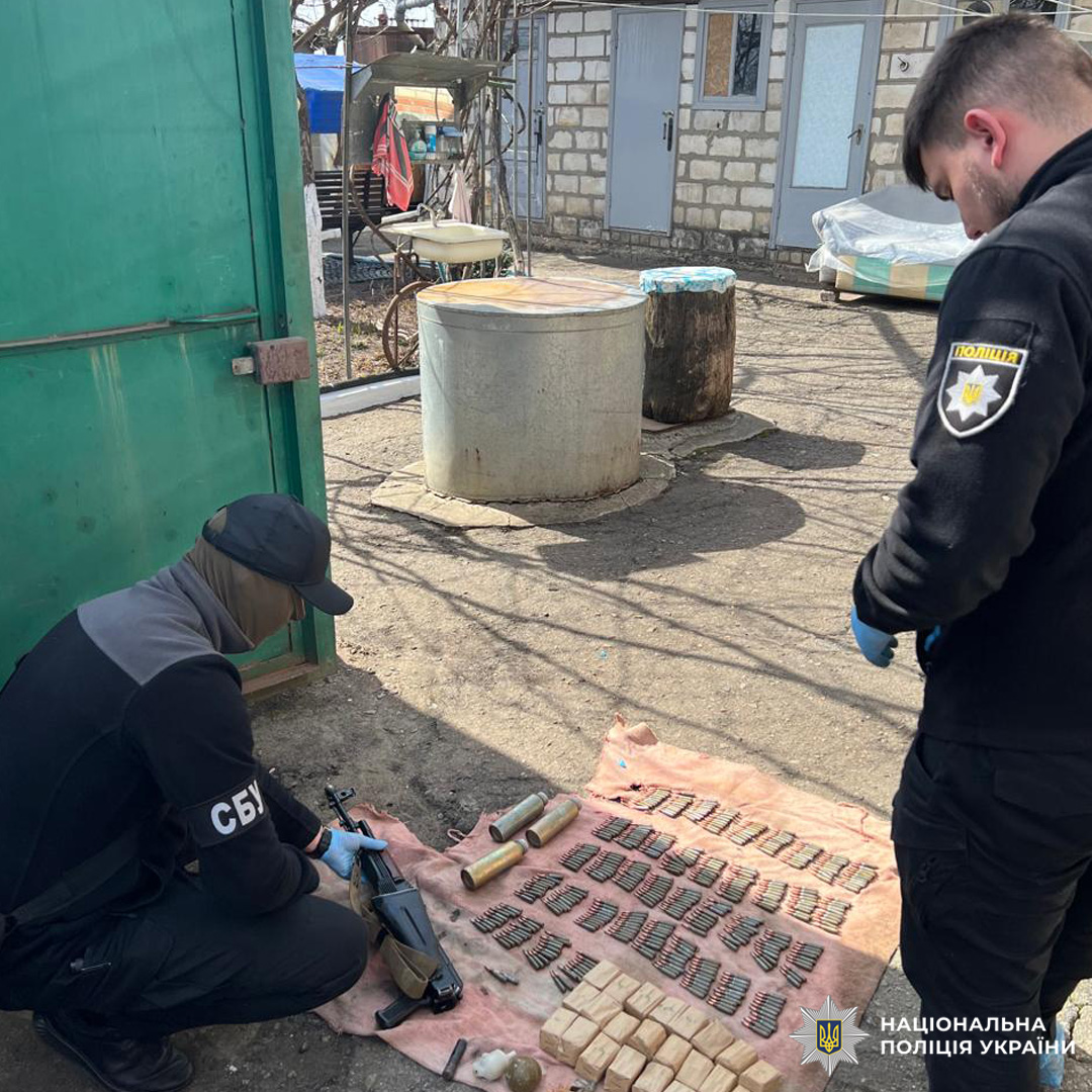 Співробітники СБУ та Національної поліції України оглядають вилучену зброю й боєприпаси, розкладені на землі.
