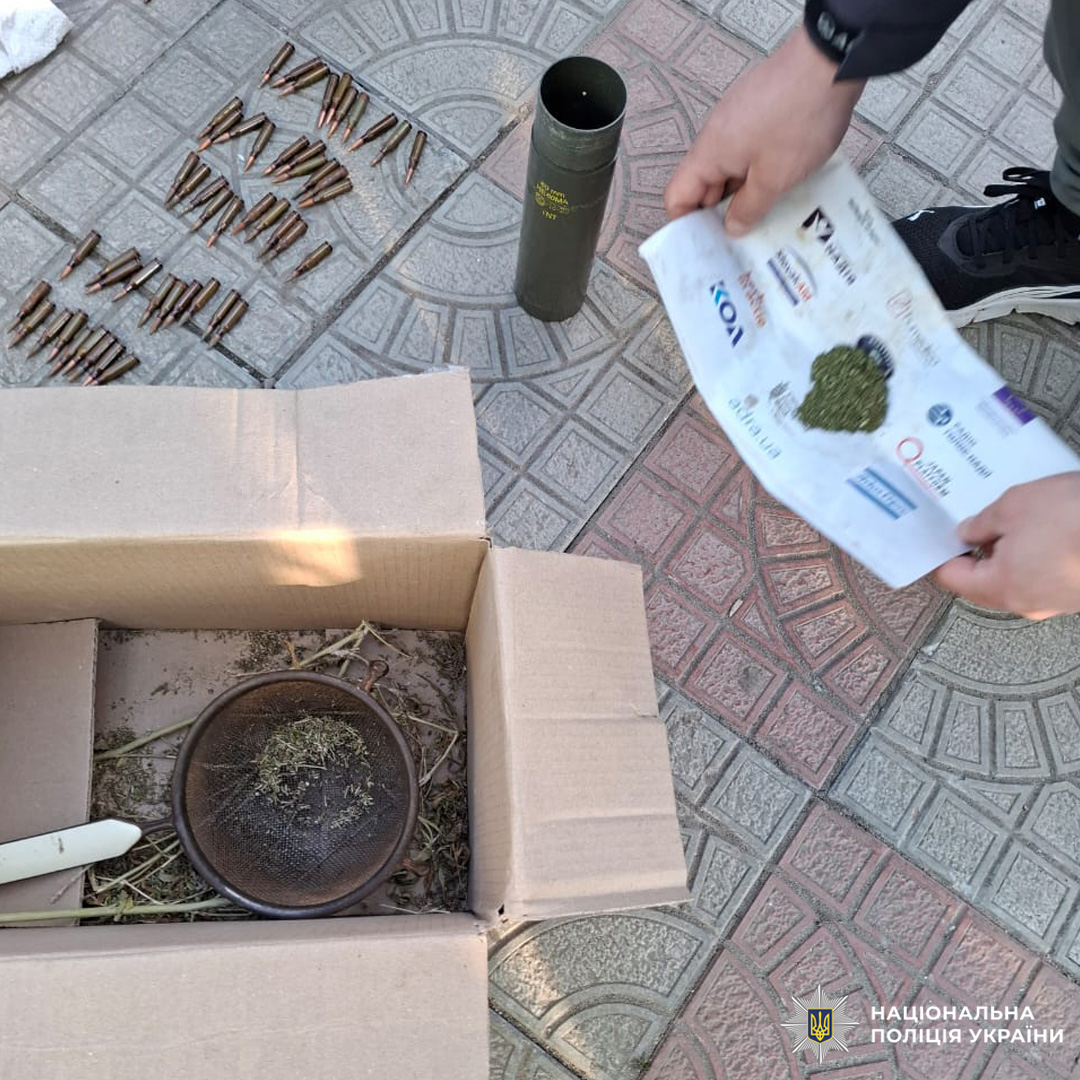 На плитці розкладені патрони, коробка з рослинною речовиною та металевими предметами, поруч зелений контейнер із маркуванням.