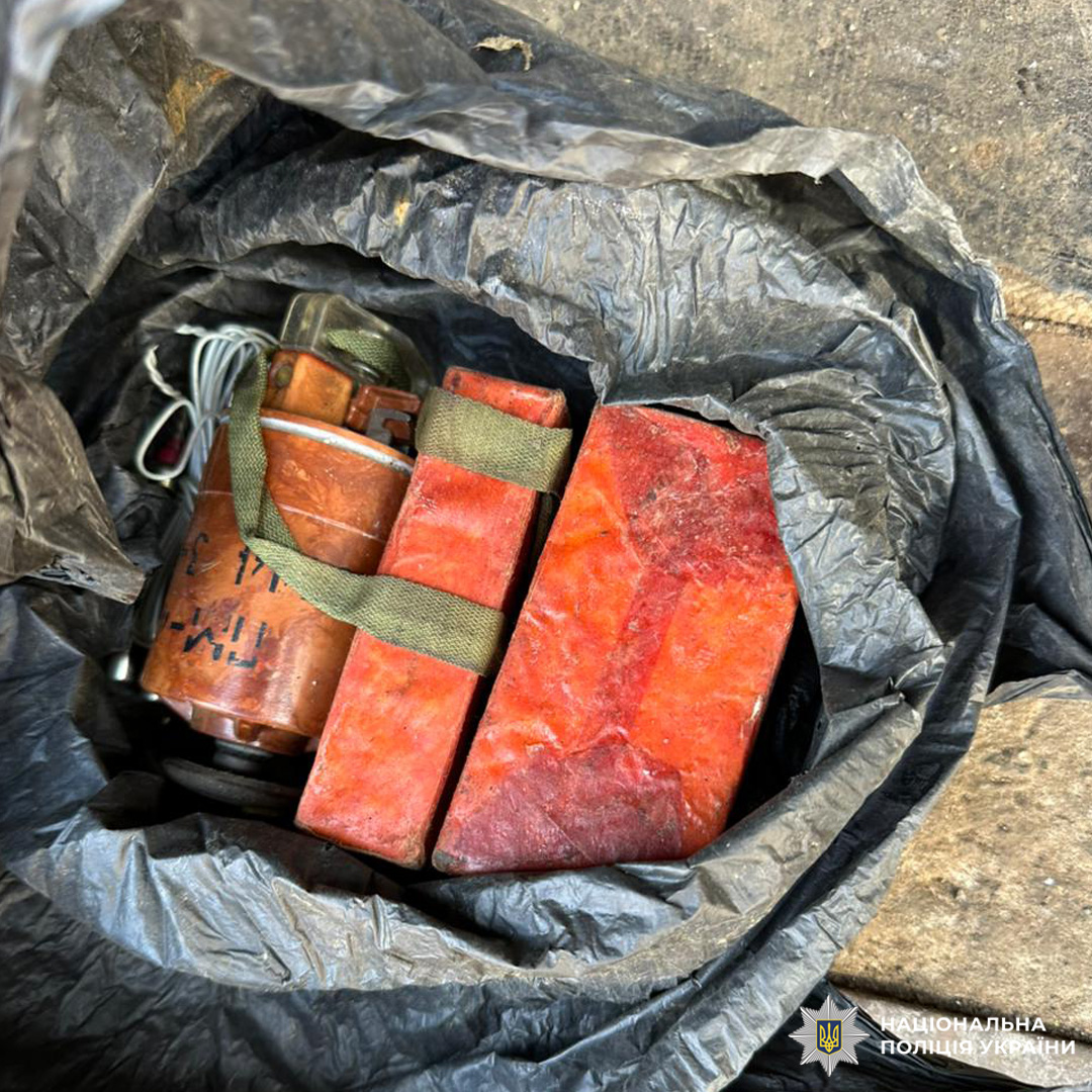 У чорному пакеті лежать червоні блоки та металевий предмет із дротами й написами, закріплений зеленим ременем.