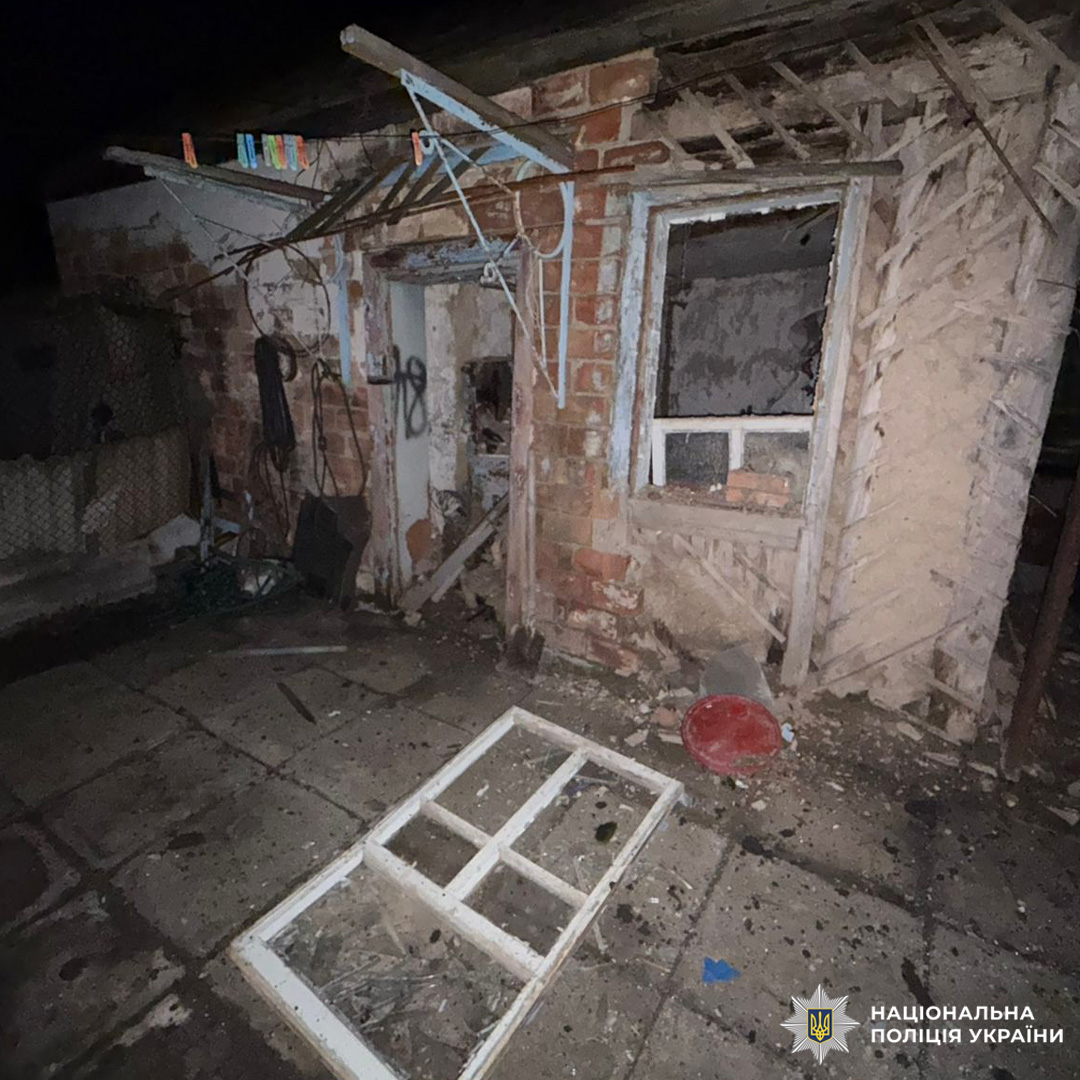 Пошкоджена цегляна будівля вночі з вибитим вікном та уламками на землі.