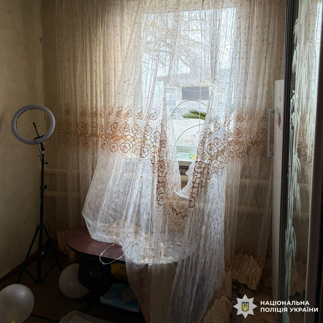 Кімната з вікном у прозорих фіранках, столом із паперами та кільцем світла на штативі.