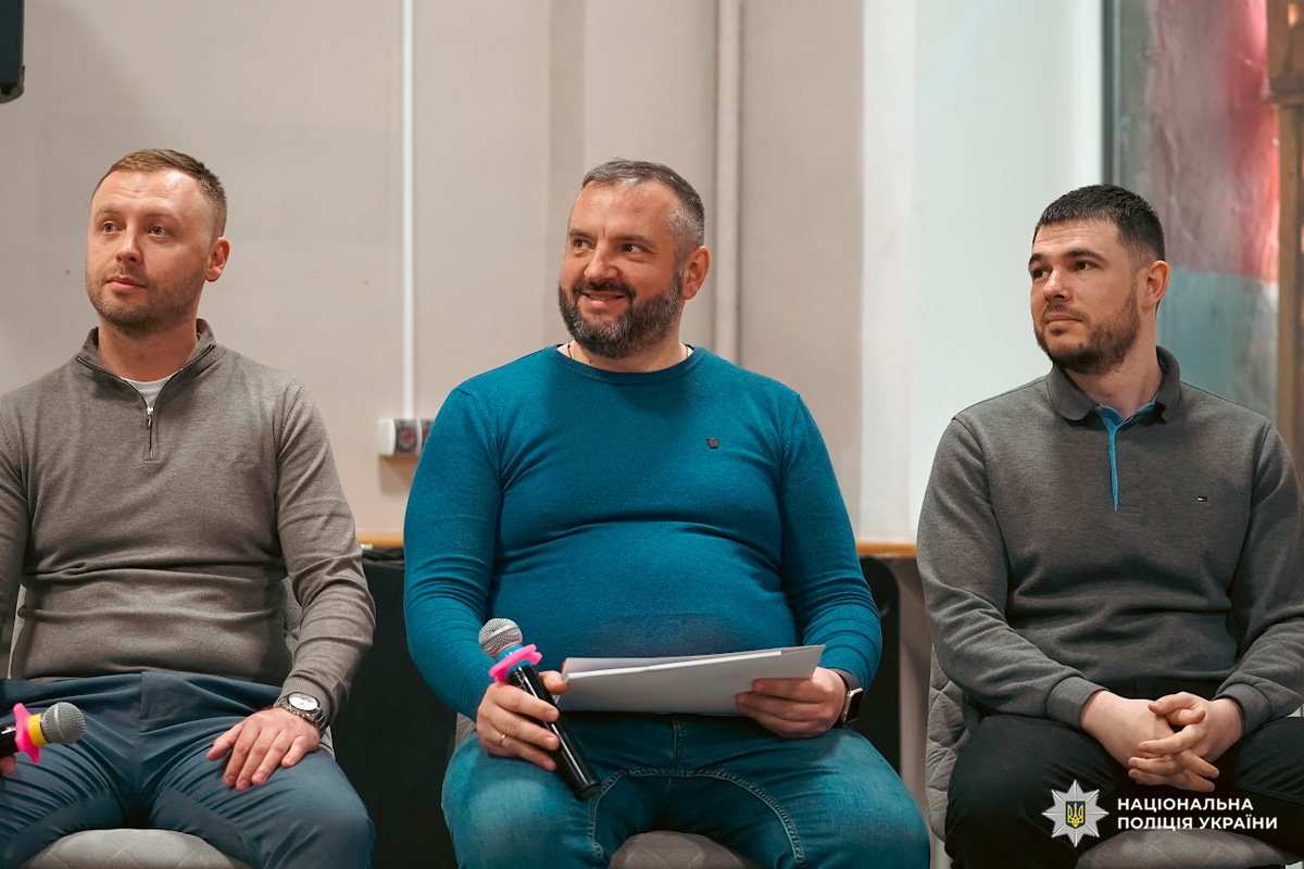 Троє учасників дискусії з мікрофонами у залі