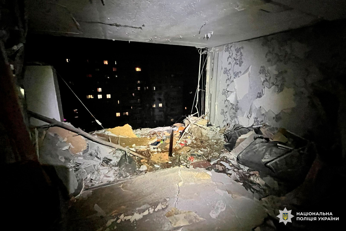 Зруйнована кімната житлового будинку: вибита стіна й вікно, уламки та дроти всередині.