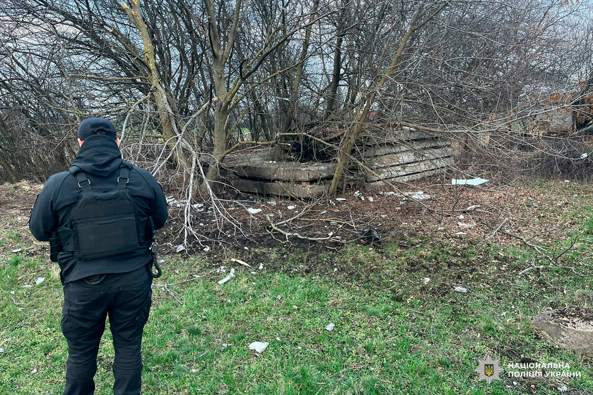 Cпівробітник поліції оглядає пошкоджену бетонну конструкцію на відкритій місцевості.