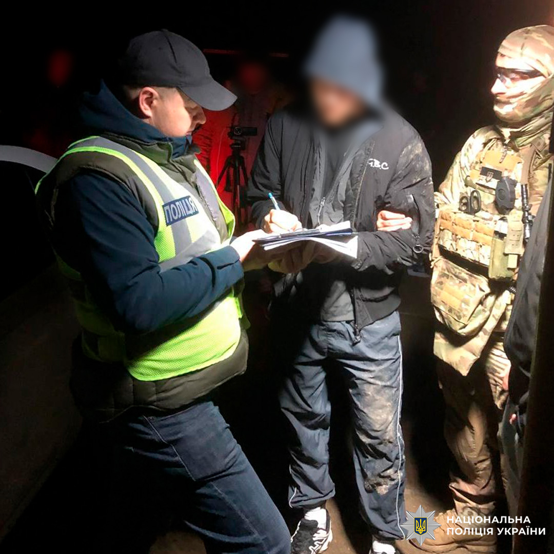 Поліцейський складає протокол, підозрюваний підписує документи, а бійці спостерігають.