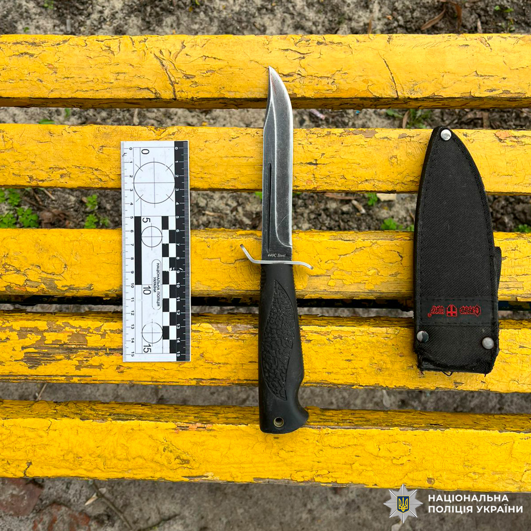 Вилучений ніж із чорним руків’ям та металевим лезом, поруч чорний чохол із червоним написом і вимірювальна лінійка для фіксації доказів.