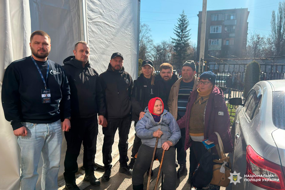 Поліцейські супроводжують літню жінку з палицями під час евакуації біля намету.