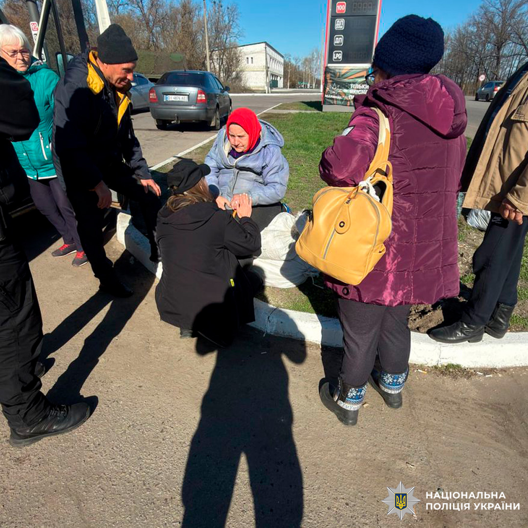 Поліцейські надають допомогу жінці, яка сидить на узбіччі, серед групи.