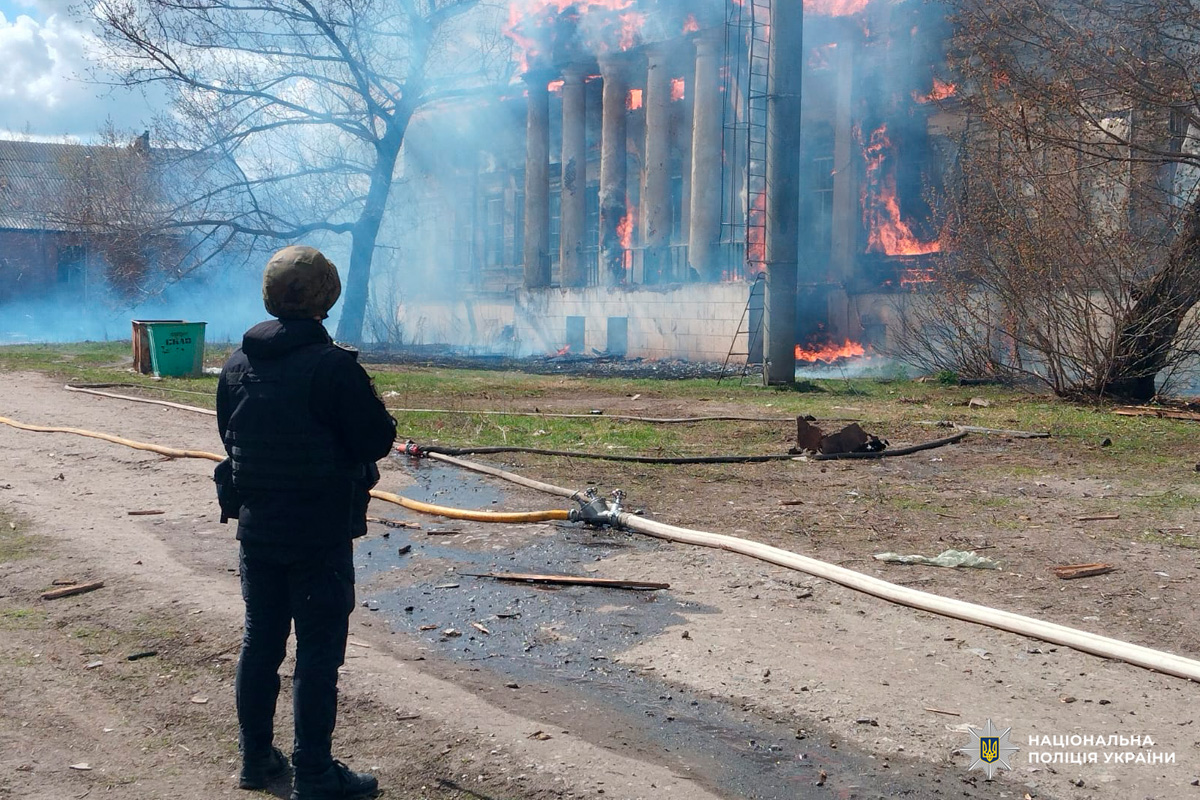 Будівля з колонами охоплена вогнем, зафіксовано масштабне займання. Поліція документує подію.