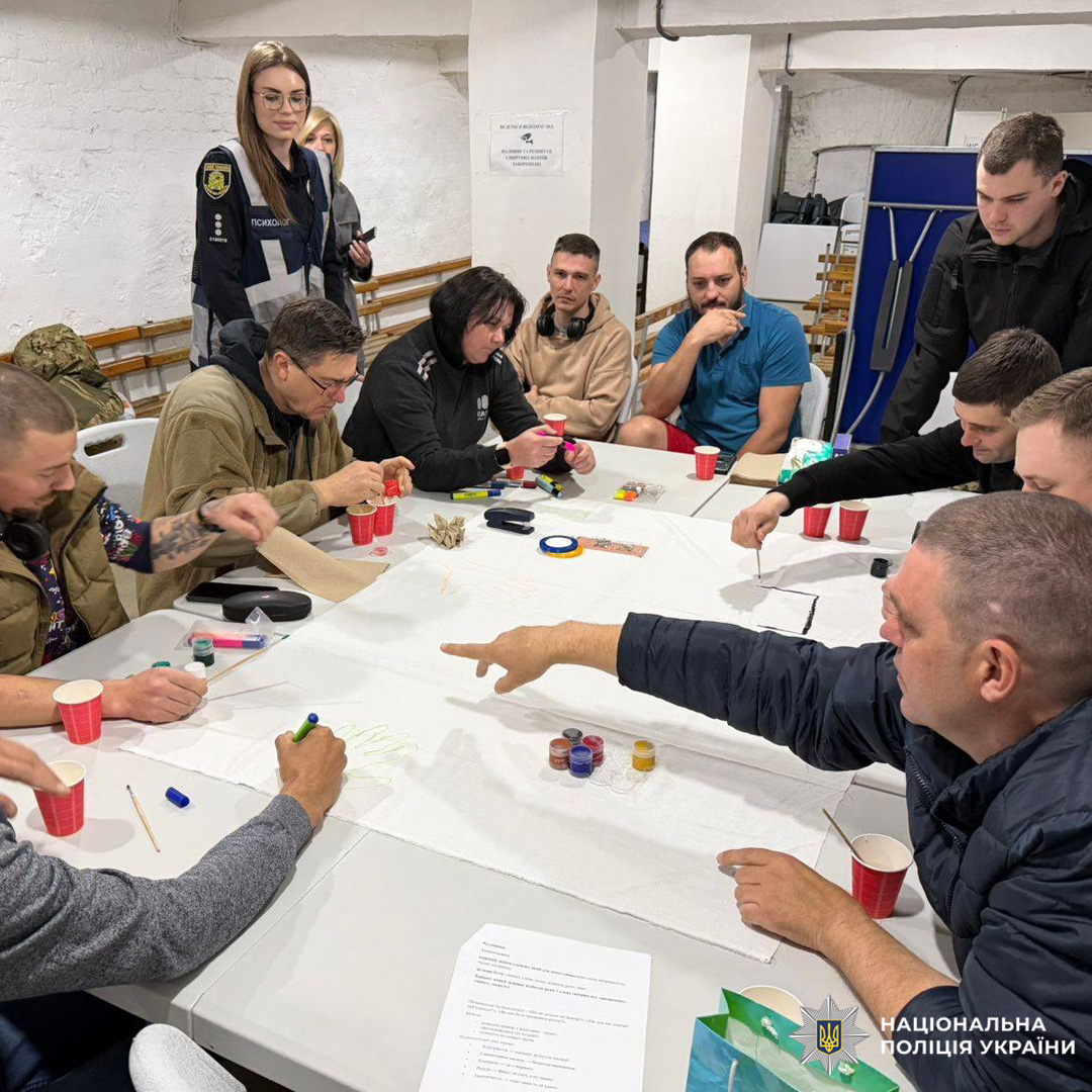 Поранені військовослужбовці беруть участь у психологічному тренінгу з елементами арт-терапії, створюючи спільне полотно з малюнками та символами.