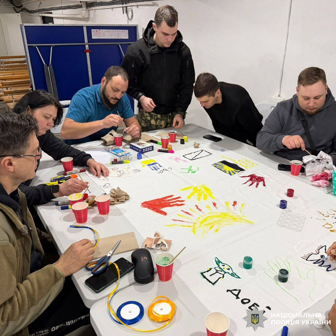 Поранені військовослужбовці створюють спільне художнє полотно з символами держави та яскравими малюнками, що символізують єдність і творчість.