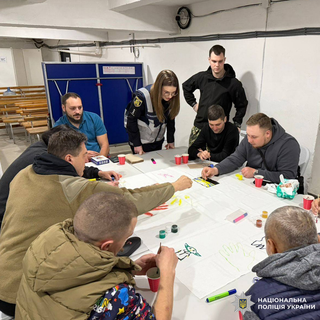 У приміщенні відбувається арт-майстерня, організована поліцією, де учасники працюють над малюнками та символами.