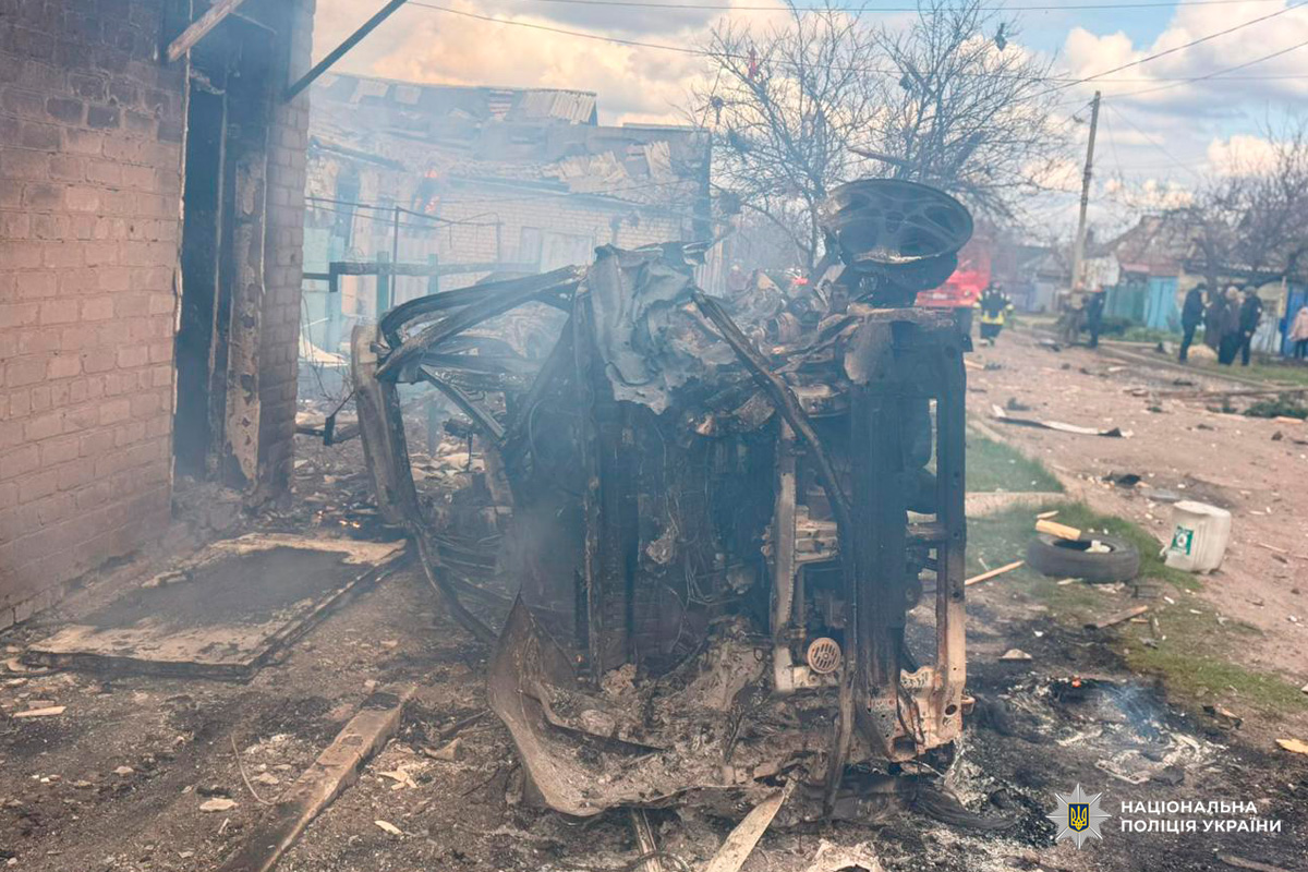 Знищений вибухом автомобіль лежить на боці біля пошкодженої будівлі, навколо уламки та сліди пожежі.