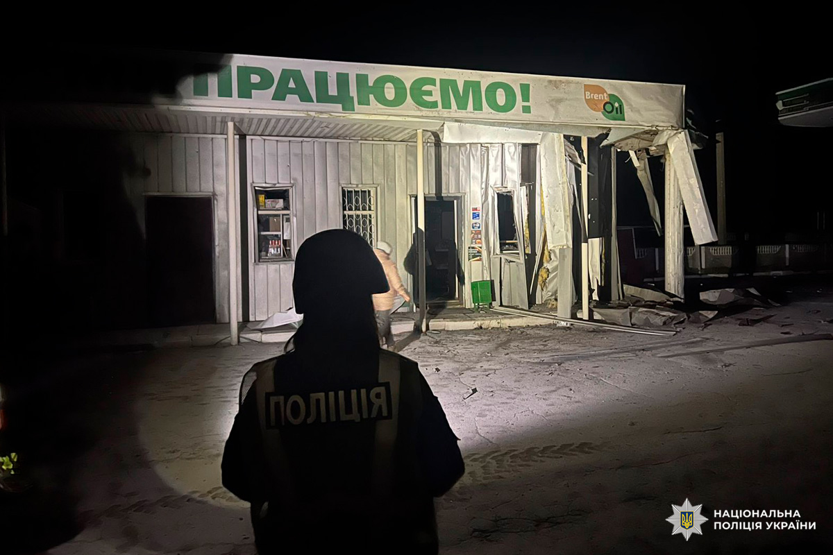 Зруйнована будівля вночі після вибуху, частини стін та даху обвалені. Поліцейський у захисному спорядженні документує наслідки.