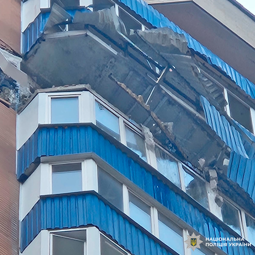 Багатоповерховий житловий будинок із серйозними пошкодженнями: обвалені балкони та фасад, уламки бетону звисають із конструкцій.