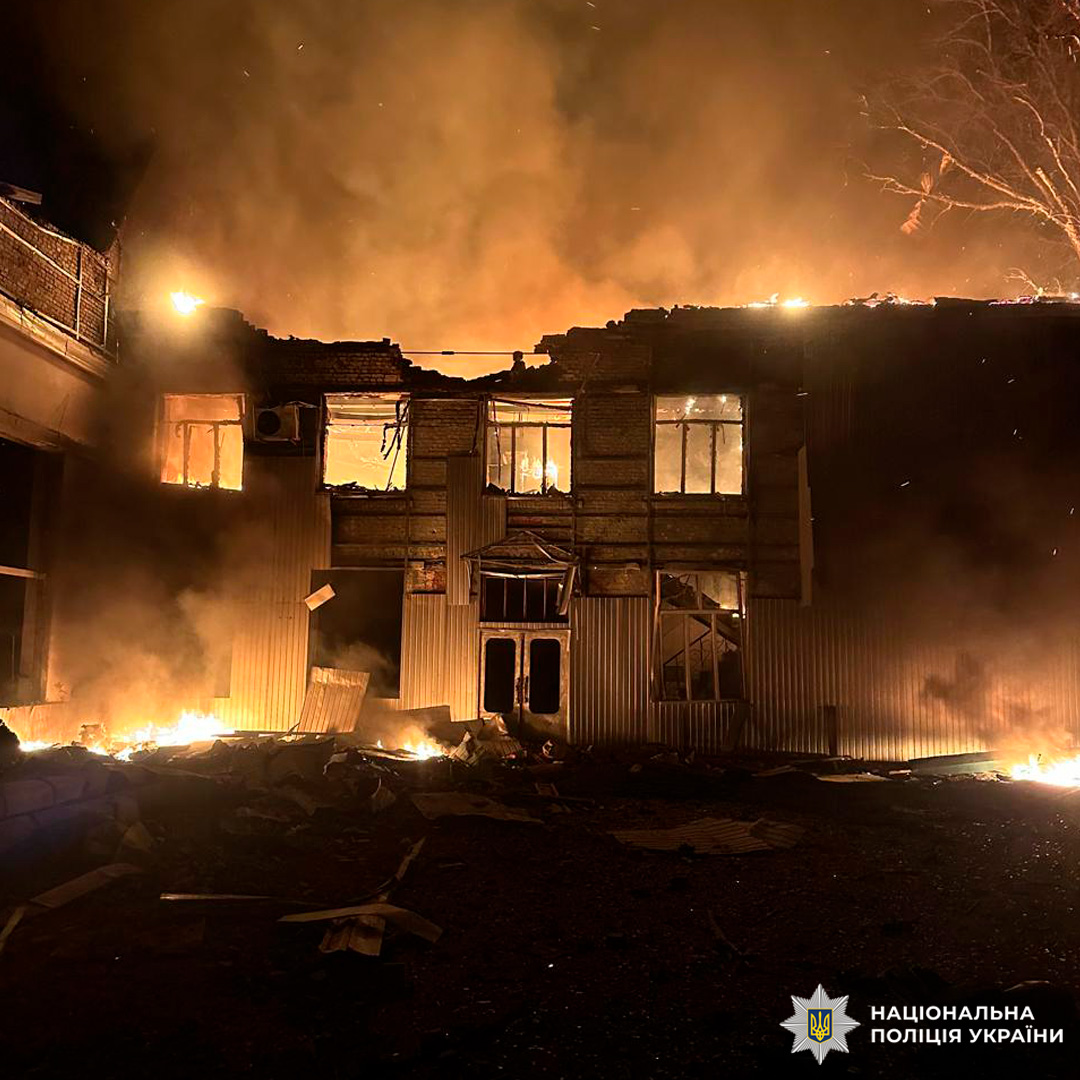 Двоповерхова будівля охоплена полум’ям уночі, дах частково обвалений, густий дим здіймається над місцем події.